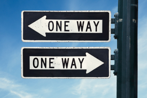 Two one-way signs on a pole pointing in different directions.