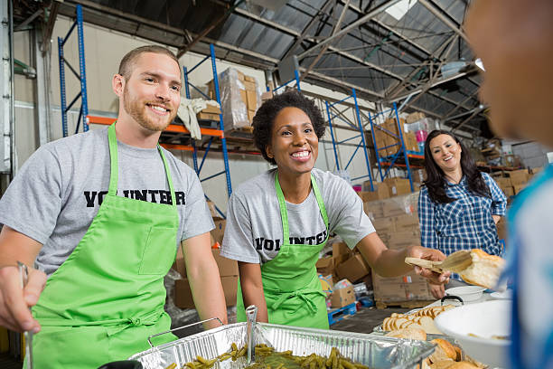 Volunteers serving hot meal to people in community soup kitchen Volunteers serving hot meal to people in community soup kitchen serving utensil stock pictures, royalty-free photos & images