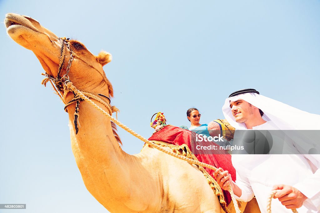 Uomo arabo e turista dorso di un cammello - Foto stock royalty-free di Adulto