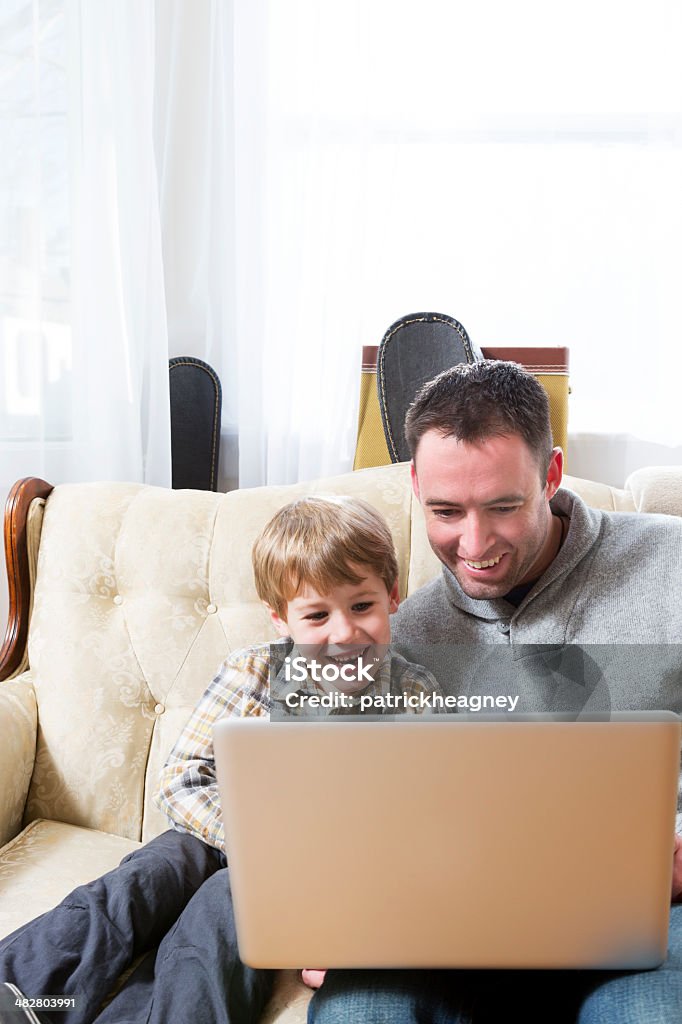 Father and Son on Laptop A father and son look at a laptop at home. Adult Stock Photo