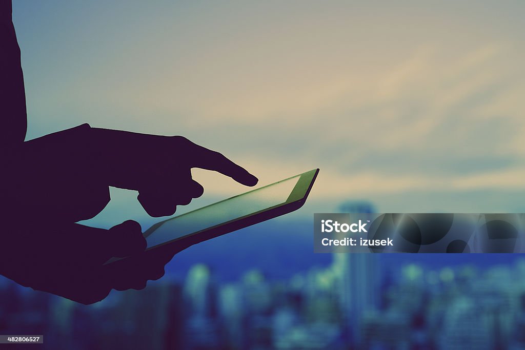 Digital tablet Close up of human finger and digital tabler with city skyline in the background. Dark tones. Digital Tablet Stock Photo
