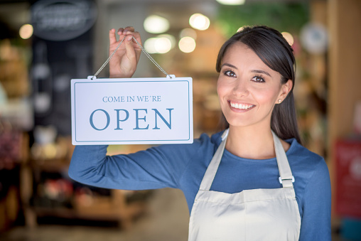 Beautiful young woman holding an open sign at a grocery store - small business concepts