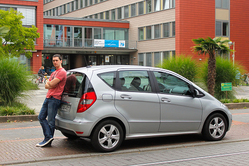 Koln, Germany — September 16, 2011: The young driver is leaning on his car Mercedes Benz A180 CDI on the background of the city street.