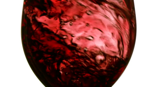 Slow motion zooming in: pouring red wine on white background