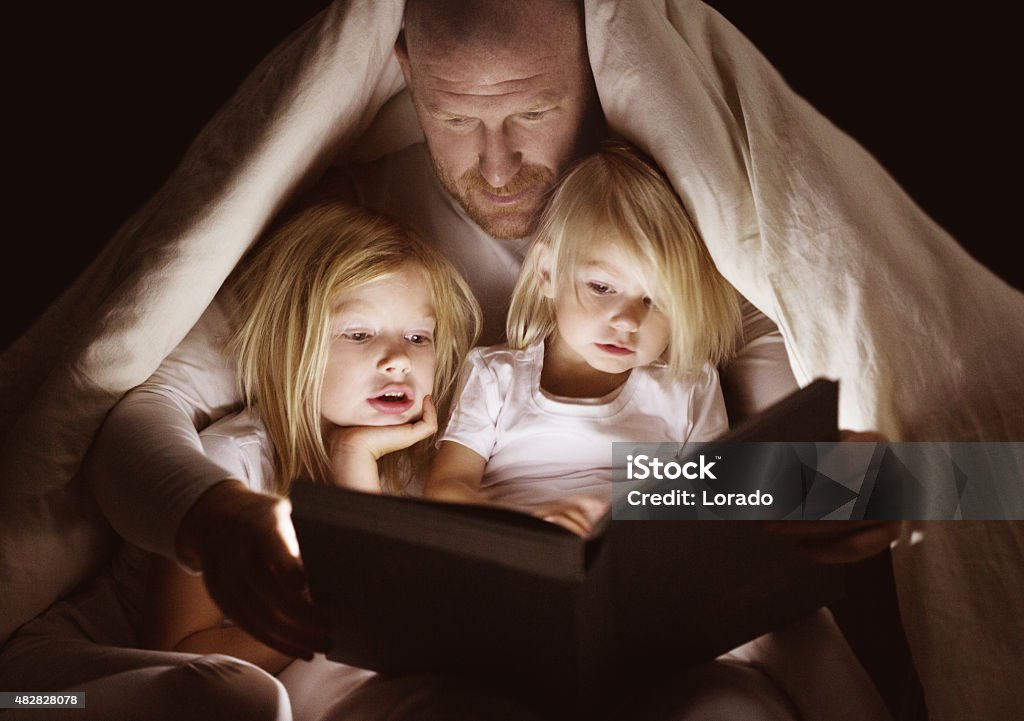 Father and daughters reading book at bedtime - Royaltyfri Historieberättande Bildbanksbilder
