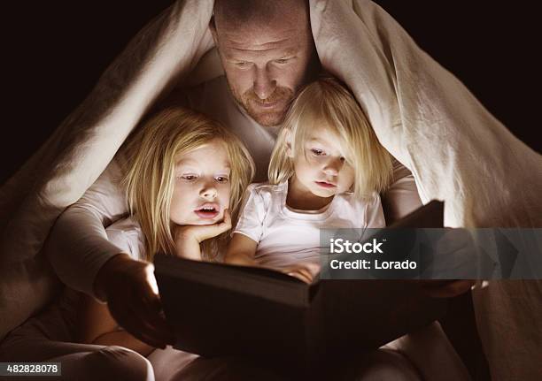 Father And Daughters Reading Book At Bedtime-foton och fler bilder på Historieberättande - Historieberättande, Bilderbok, Saga
