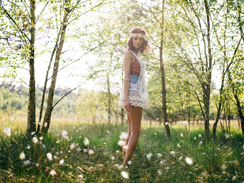 Hippie girl in a summer park with wild white flowers growing in the grass around her looking back at the camera