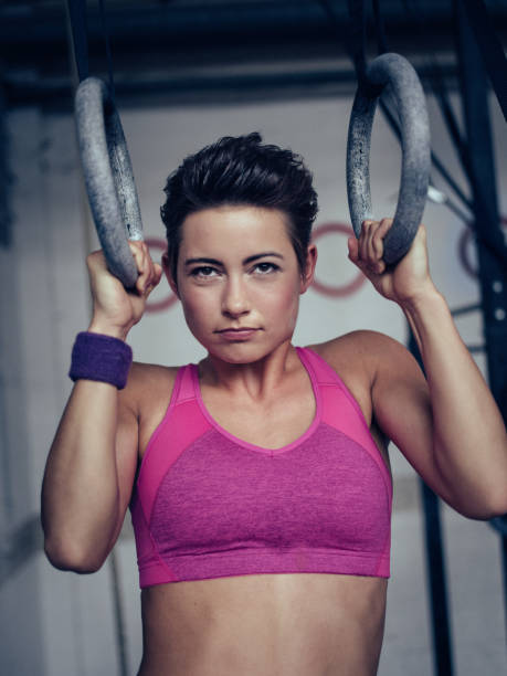 Girl doing pull-ups with gymnastic rings looking intense Teen girl with an intense expression doing pull-ups in a gym on gymnastic rings crossfit girl stock pictures, royalty-free photos & images