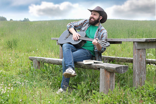 guitarrista en un sombrero de vaquero en la naturaleza - cowboy blue meadow horizontal fotografías e imágenes de stock