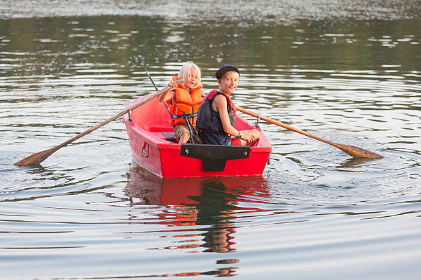 Two young brothers in red bowing boat. Sweden Both have life jackets. The younger one is rowing. Stockholm Archipelago, Sweden.