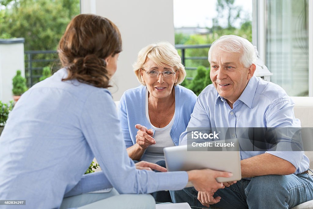 Senior couple talking with insurance agent Cheerful senior couple having meeting with financial advisor or insurance agent at home. Advice Stock Photo