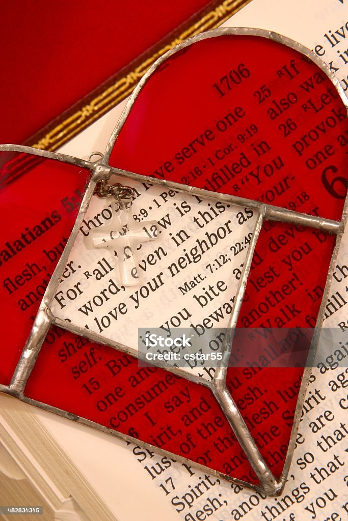 Religious: Love Your Neighbor Bible Scripture with stained glass heart Bible opened to Scripture in Galatians saying "Love your neighbor" in the center of a red stained glass heart with crystal cross. Vertical Christian image. Art And Craft Stock Photo