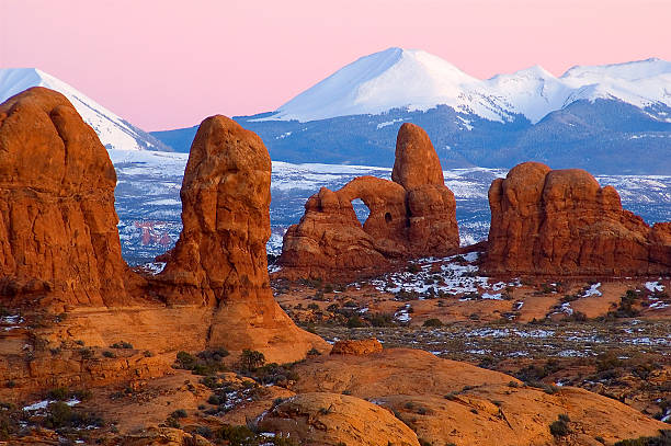 Arches and La Sals Turret Arch in the foreground and the La Sal Mountains in the background.  An early dawn winter photo in Arches National Park, Utah. la sal mountains stock pictures, royalty-free photos & images