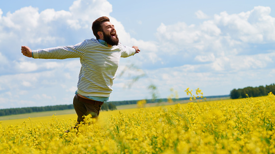 Ecstatic young man running across blossoming summer meadow