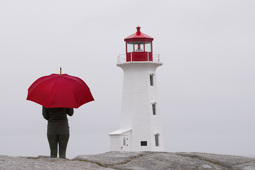 A young woman (my daughter) holding a red umbrella at the lighthouse in Peggy's Cove, Nova Scotia, Canada