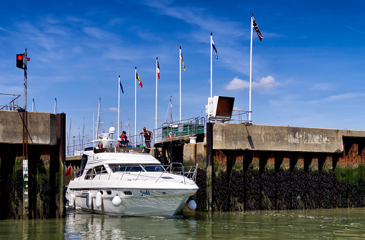 Shotley Gate, Suffolk, England - May 27, 2015: A small motor cruiser, with people on board and more people watching from the quayside, passing through the lock which connects Shotley Marina with the River Orwell estuary in Suffolk, eastern England. The estuary is tidal so the lock is necessary to regulate the respective heights of the marina and the harbour.