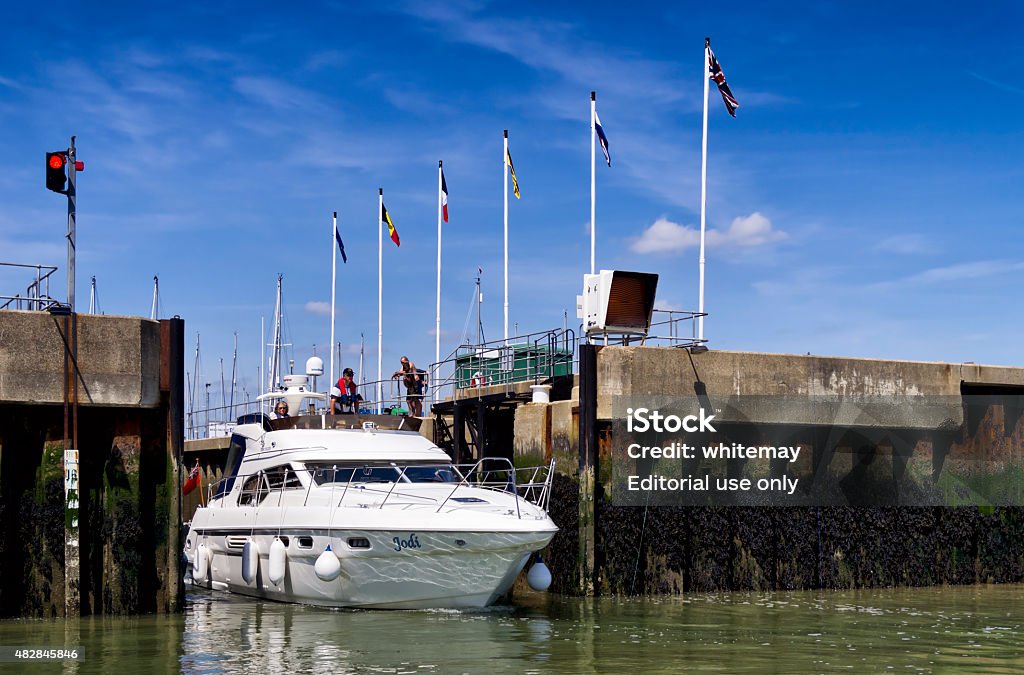 Pleasure craft passing through lock gates Shotley Gate, Suffolk, England - May 27, 2015: A small motor cruiser, with people on board and more people watching from the quayside, passing through the lock which connects Shotley Marina with the River Orwell estuary in Suffolk, eastern England. The estuary is tidal so the lock is necessary to regulate the respective heights of the marina and the harbour. 2015 Stock Photo