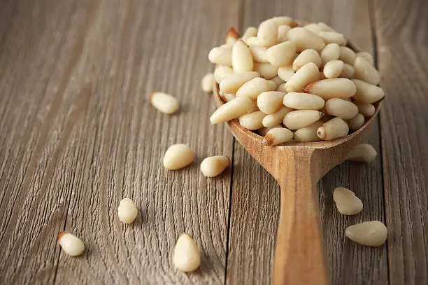 Peeled pine nuts in wooden spoon on wood background.