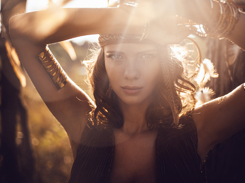 Portrait of a beautiful wild girl standing a summer field in golden afternoon sun flare