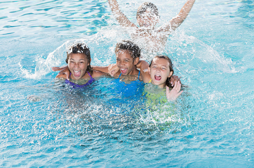 Multi-ethnic group of children (9 to 13 years) playing in swimming pool, splashing.