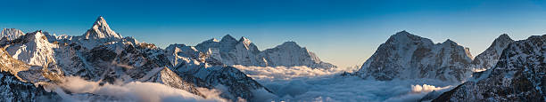 Magnificent mountain panorama snowy peaks high above clouds Himalayas Nepal The iconic snow capped spire of Ama Dablam illuminated by the golden light of a high altitude sunset overlooking the clouds in the Khumbu mountain valley below, Mt. Everest National Park, Himalayas, Nepal. ProPhoto RGB profile for maximum color fidelity and gamut. base camp photos stock pictures, royalty-free photos & images