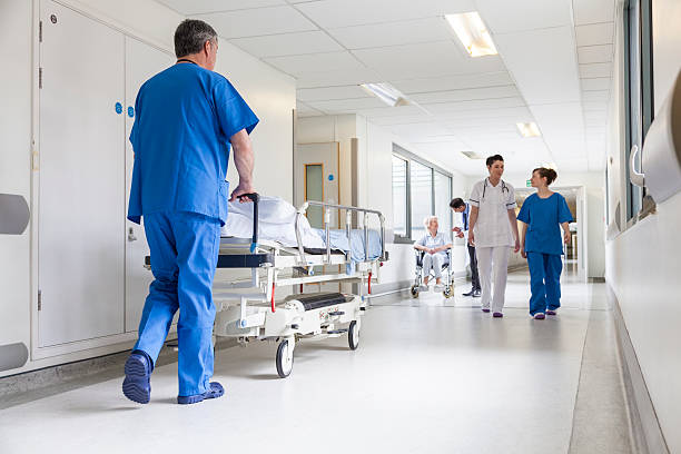 Doctors Hospital Corridor Nurse Pushing Gurney Stretcher Bed Male nurse pushing stretcher gurney bed in hospital corridor with doctors & senior female patient hospital stock pictures, royalty-free photos & images