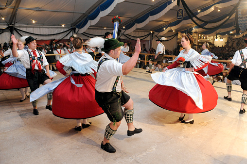 Garmisch, Germany - July 31, 2010: Every year many customs folk festivals take place in Bavaria for local people and tourists in big tents. While the guests drink beer, members of a local dancing group make a show on stage. They are dressed in traditional bavarian clothes - mens with feather on hat, white shirt, the world famous short leather trousers with decorated suspenders and the cutted socks on legs - women with shawl and wide skirt named Dirndl. The famous dance, named Schuhplattler, works that men clap with their hands to legs, shoes and trousers, so every stroke gaves a loud bang in rhythm of music. Women tourn around herself all the time.