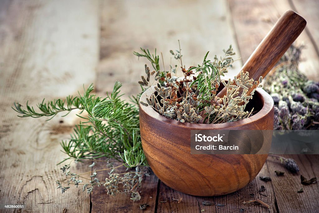 Herbs in mortar with pestle on the table Fresh herbs inside a wooden mortar and pestle bowl on a wooden plank table with knotholes and nails.  The herbs have multiple colors and textures.  The bowl has a swirl pattern and is surrounded by piles of additional fresh herbs. Mortar and Pestle Stock Photo