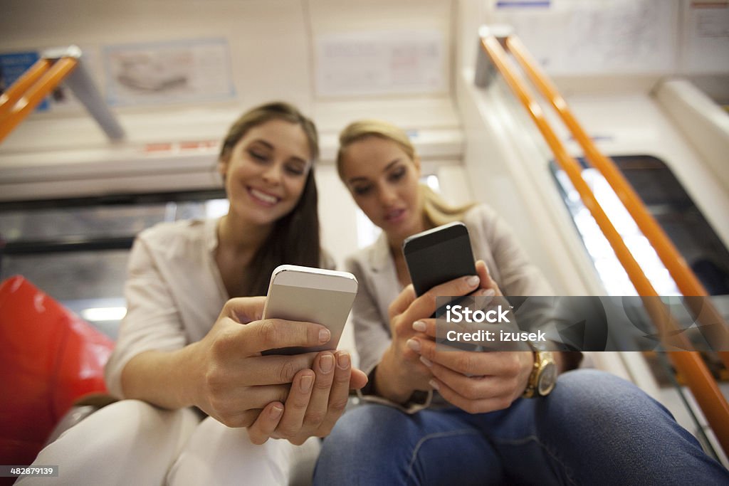 Friends in London Overground Two smiling young women sitting in a London overground train and using their smart phones. Close up on human hands. Mobile Phone Stock Photo