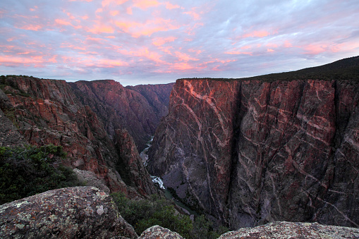 Sun rises over Black Canyon of the Gunnison, Colorado. This cliff is the Painted Wall, the tallest vertical cliff in Colorado, at 2,722 feet. Sunlight barely peeks through the clouds to brighten the top of the cliff with a touch of sunlight.