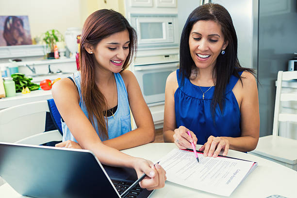 Mother helping daughter fill out College Applications in the Kitchen Mother and teenage daughter are in the kitchen researching colleges and filling out university applications. form document stock pictures, royalty-free photos & images