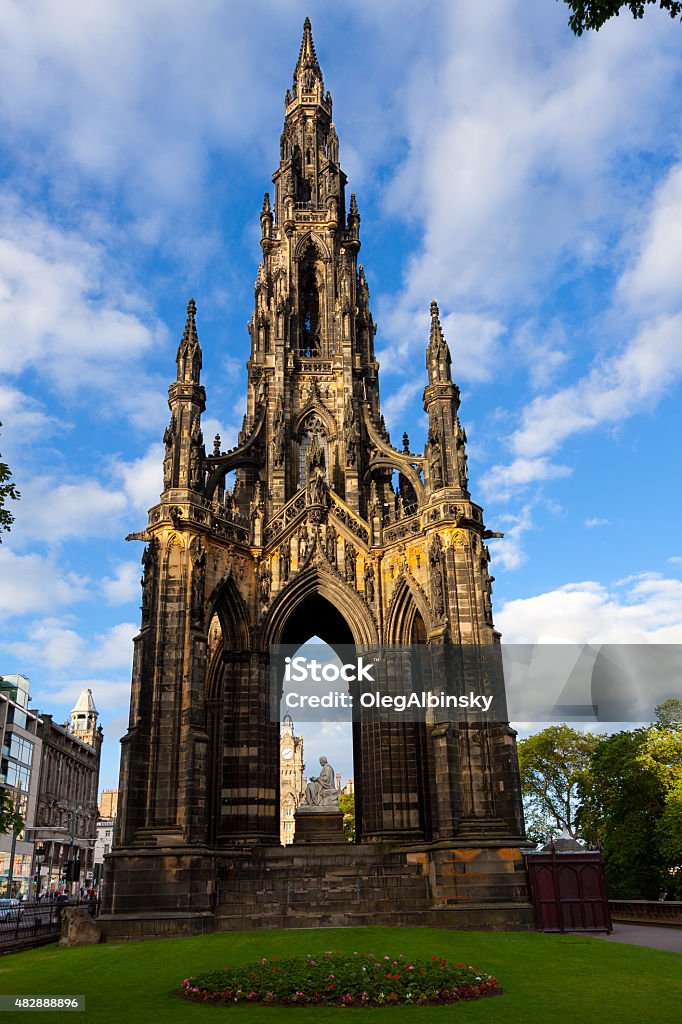 Scott Monument in Edinburgh, Scotland, United Kingdom. The Scott Monument in Edinburgh, Scotland, United Kingdom. It is a Victorian Gothic monument to Scottish author Sir Walter Scott and is the largest monument to a writer in the world. The image taken from Princes Street Gardens. Green trees and Blue sky with clouds are in background. This HDR photorealistic image is taken in the evening at sunset. Canon EF-S 10-22 mm f/3.5-5.6 wide angle lens. Edinburgh - Scotland Stock Photo