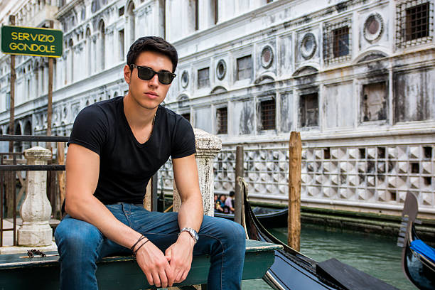 Portrait of Attractive Dark Haired Young Man Leaning Against Railing on Foot Bridge Over Narrow Canal in Venice, Italy