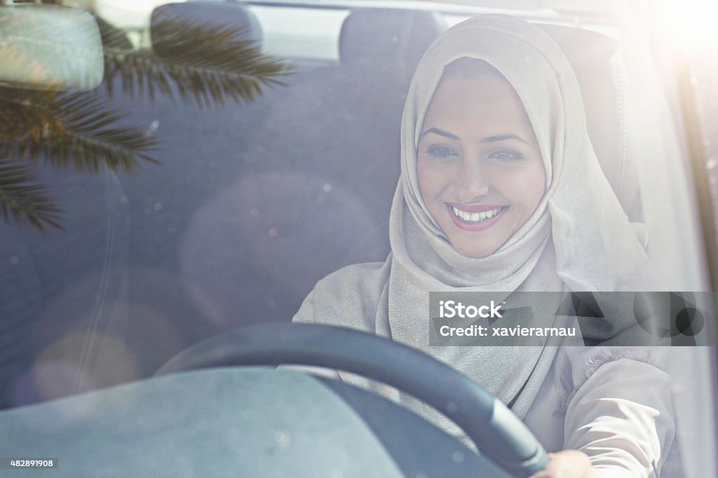 Emirati woman driving a car Portrait of a Middle Eastern woman driving a car, she is wearing a modern beige Abaya. Driving Stock Photo