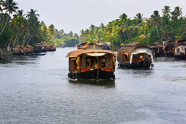 Kochi, India - April 22, 2009: Houseboats move along a canal at the Kerala Backwaters, near Kochi, Kerala state, India. Also called kettuvallams they are one of the prominent tourist attractions in Kerala, used as moving accomodations.