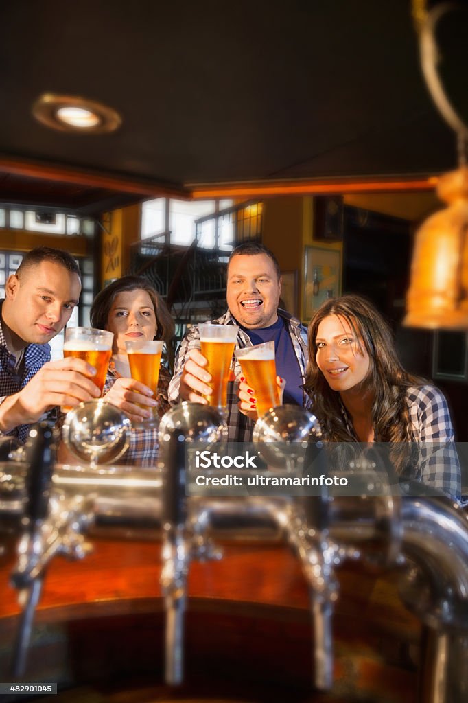 Friends in a pub Group of friends  enjoying in beer.In the foreground, pouring beer on tap in the old pub. The grain and texture added. Very shallow DOF . Adult Stock Photo