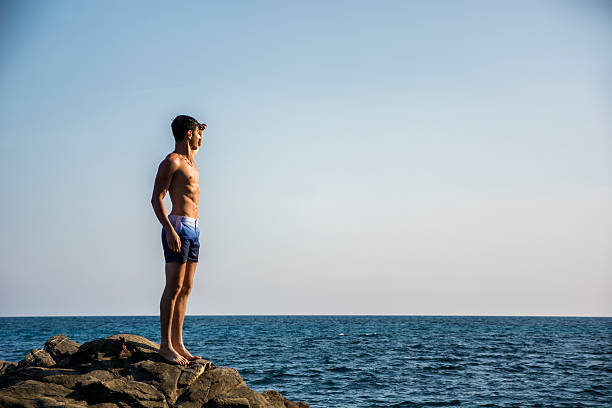 istock Muscular young man on rock by sea 482901282