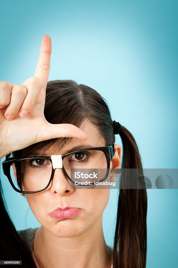 Sad, Nerdy Young Woman Making an 'L' on Her Forehead Color photo of a sad, nerdy young woman making an 'L' on her forehead. 25-29 Years Stock Photo