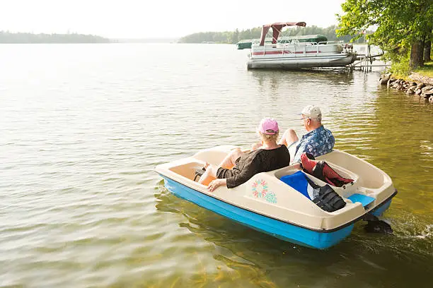 Senior Caucasian couple in their 70's use foot pedals to move a paddleboat across the water on a sunny summer day, Ten Mile Lake, Walker, MN, USA