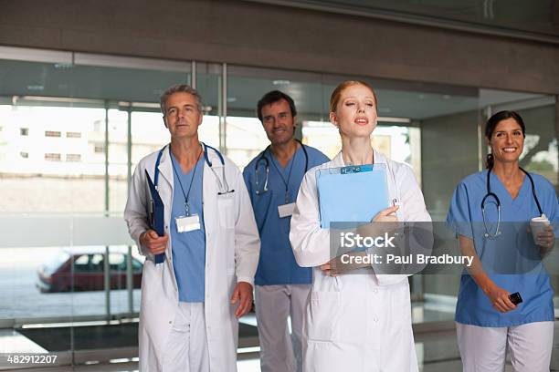 Four Hospital Workers Walking In Corridor Holding Clipboards And Smiling Stock Photo - Download Image Now