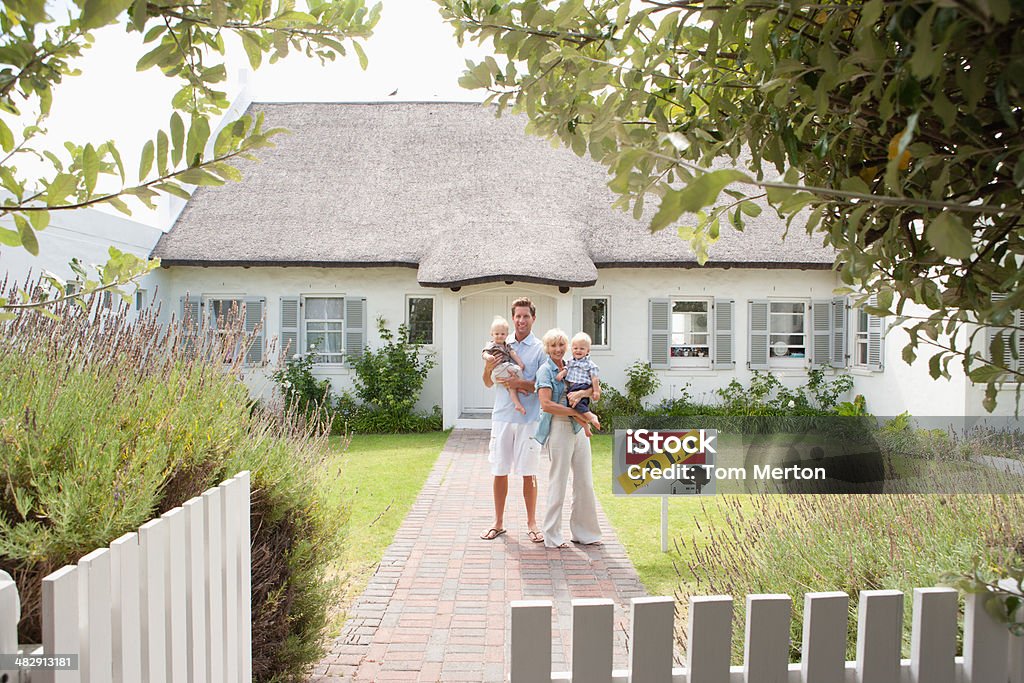 Man and woman holding babies in front of house with sold sign and white fence  Family Stock Photo