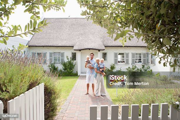 Man And Woman Holding Babies In Front Of House With Sold Sign And White Fence Stock Photo - Download Image Now