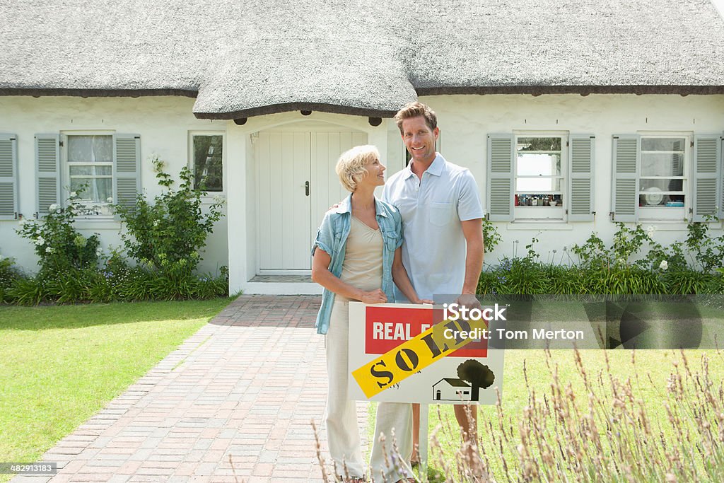 Man and woman outdoors in front of house with sold sign  House Stock Photo