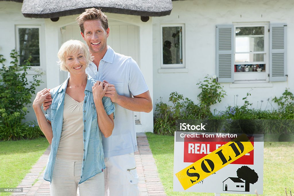 Man and woman outdoors in front of house with sold sign  Couple - Relationship Stock Photo