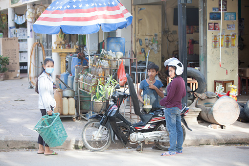 Siem Reap, Cambodia - July 6, 2014: Boy refueling woman's motorbike from the bottle on traditional asian gas station.