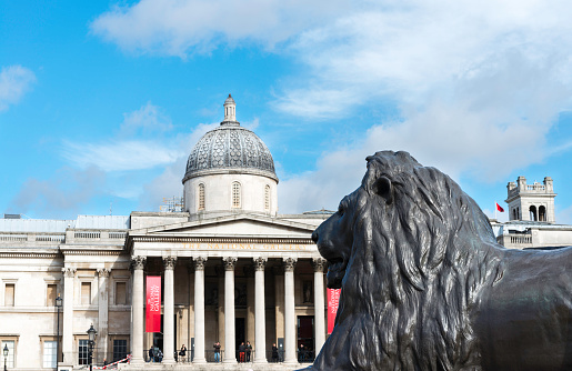 London, United Kingcom - March 22, 2014: Groups of tourists and locals enjoy the sunshine at the main entrance to the National Gallery in Trafalgar Square, with lion from Admiral Nelson column in the foreground. The gallery houses the national collection of western european painting.
