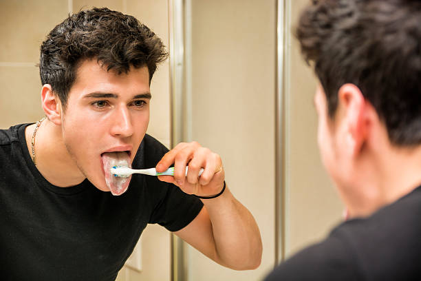 headshot of attractive young man brushing teeth and tongue - mensentong stockfoto's en -beelden