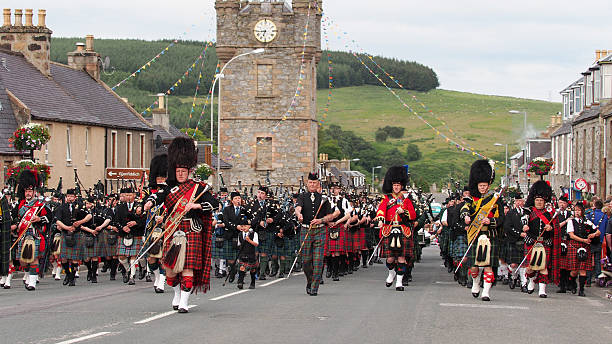 Massed Pipe Bands marching in Dufftown, Scotland. Dufftown, Scotland - July 25, 2015: Massed Pipe Bands "Beating the Retreat" in the town centre to mark the end of the Highland Games in Dufftown, Scotland.  Massed pipe bands are a feature of the Scottish Highland Games, which are a popular tourist attraction during the summer. sporran stock pictures, royalty-free photos & images