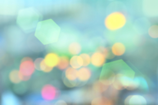 Blurred cityscape background at night, with defocused green, blue and yellow bokeh street lights. Soft hues and pastel colors, with lens flare.