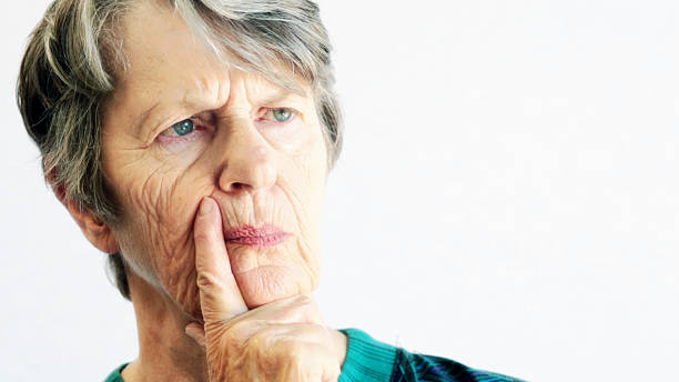 Pensive old woman thinking things over A thoughtful old wman tapping her face with her index finger, frowns slightly as she thinks. Copy space to the side. looking around stock pictures, royalty-free photos & images